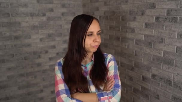 En vacker ung kvinna i rutig skjorta är på dåligt humör. En ung kvinna visar en förolämpning på en tegelsten bakgrund. — Stockvideo