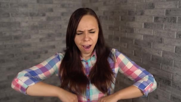 Krásná mladá žena v kostkované košili zívá z únavy na cihlovém pozadí. — Stock video