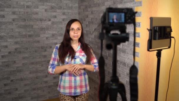 Μια νεαρή γυναίκα με καρό πουκάμισο μιλάει μπροστά στην κάμερα σε ένα φόντο από τούβλα. Μια γυναίκα blogger οδηγεί το vlog της. — Αρχείο Βίντεο