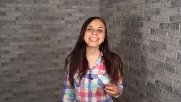 Una joven de una camisa de camisa está hablando a puerta cerrada sobre un fondo de ladrillo. Una bloguera mujer lidera su anzuelo. — Vídeos de Stock