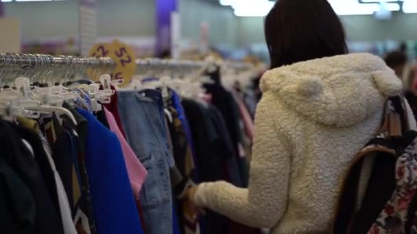 Κορίτσι για ψώνια. Πορτρέτο μιας όμορφης γυναίκας στο μαγαζί. Κορίτσι στο κατάστημα ψάχνει για ρούχα για να αγοράσει. Νεαρή γυναίκα ψωνίζει ρούχα — Αρχείο Βίντεο