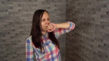 Ekose gömlekli güzel bir kadın tuğla bir arka planda yorgunluktan esniyor..