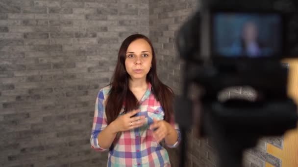 Una joven de una camisa de camisa está hablando a puerta cerrada sobre un fondo de ladrillo. La mujer está grabando contenido para su registro. — Vídeo de stock