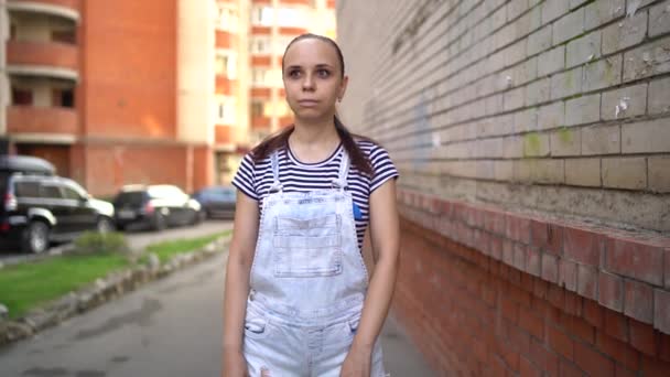 Een jonge vrouw kijkt in angst rond. Een emotionele vrouw in casual kleding kijkt verdacht rond in de straat. — Stockvideo