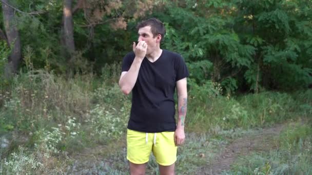 En ung stilig man i vardagskläder kliar sig i hakan och ser sig omkring i skogen.. — Stockvideo