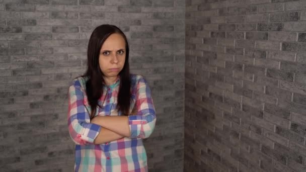 A beautiful young woman in a plaid shirt is being in bad mood. A young woman shows an insult on a brick background. — Stock Video