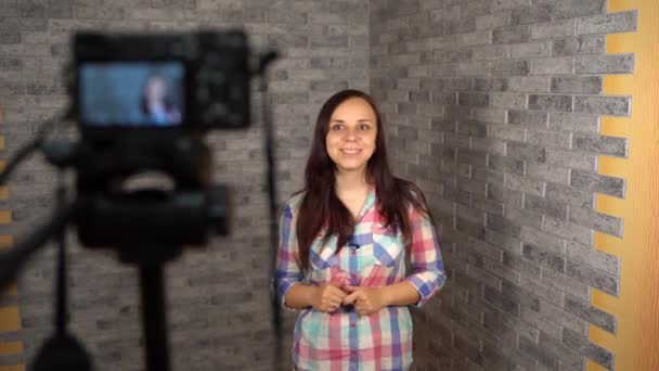 Молода жінка в плетеній сорочці говорить на камеру на цегляному фоні. Молода жінка записує відео для свого входу на цифрову камеру . — стокове відео