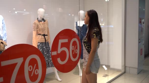 시즌 세일, 검은 금요일 쇼핑 컨셉. 가게 진열창에 서 있는 가격 의 50% 를 할인 한다는 표시입니다. 젊은 여자는 옷을 싼 값에 선택 한다. 옷을 입은 마네킹을 보는 여자 — 비디오