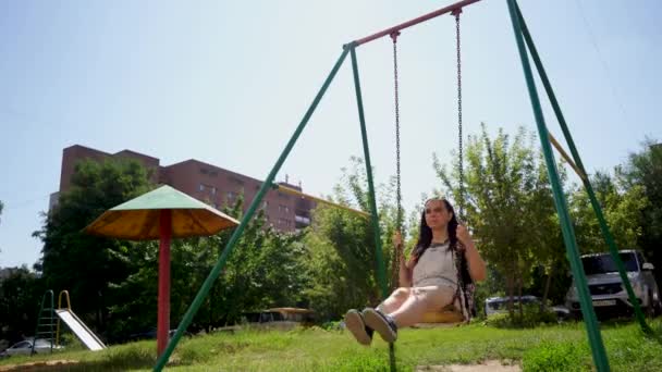 A young woman in casual clothes is swinging on a swing on the playground. — Stock Video