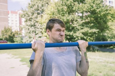 Gündelik giysiler içinde genç yakışıklı bir adam yatay çubuk üzerinde egzersiz yapıyor. fitness, spor, egzersiz, eğitim ve yaşam tarzı konsepti - genç adam barfiks çekiyor