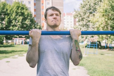 Gündelik giysiler içinde genç yakışıklı bir adam yatay çubuk üzerinde egzersiz yapıyor. fitness, spor, egzersiz, eğitim ve yaşam tarzı konsepti - genç adam barfiks çekiyor