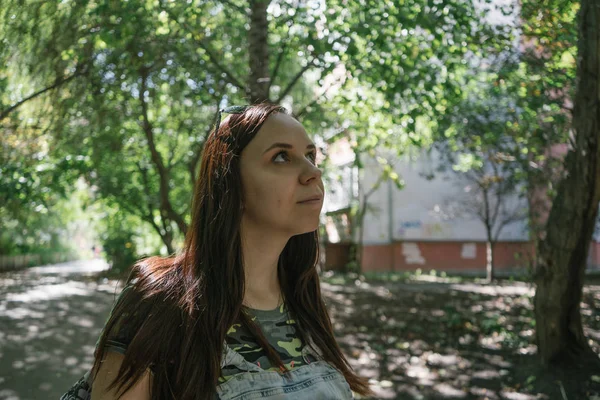 Uma jovem em roupas casuais está sorrindo e olhando para o topo no parque. — Fotografia de Stock