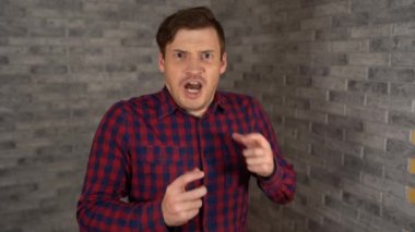 Gündelik giysiler içinde genç yakışıklı bir adam tuğla bir arka planda korku gösteriyor. Bir adam korkuya kapıldı..