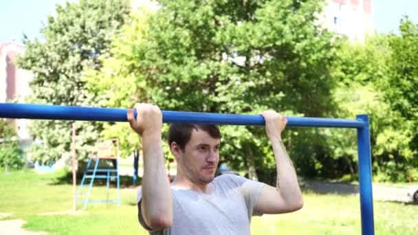 Un joven guapo con ropas casuales está haciendo ejercicio en la barra horizontal. El concepto de humor, chistes y deportes.. — Vídeos de Stock