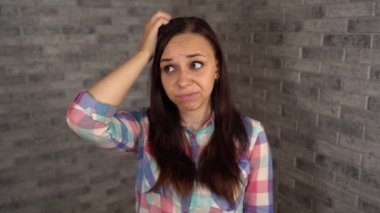 Ekose gömlekli güzel duygusal bir kadın kafasını tuğla bir arka planda kaşıyor..