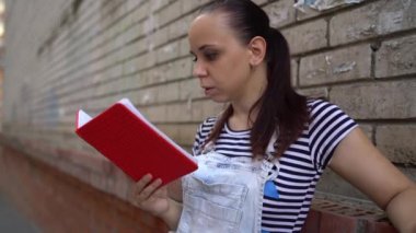 Günlük giysiler içinde güzel bir genç kadın günlüğe bakar, sokakta duvara yaslanır..