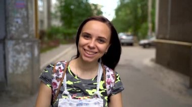 Gündelik giysiler içinde güzel bir genç kadın sokakta gülümsüyor. Uzun saçlı esmer rüzgârda ağır çekimde gelişir..