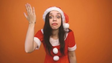 Noel Baba kostümüyle gülümseyen genç bir kadın turuncu arka planda hediyeler tutuyor. Mutlu Noeller ve mutlu yıllar..