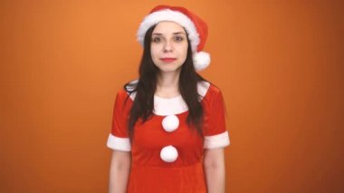 Noel Baba kostümüyle gülümseyen genç bir kadın turuncu arka planda hediyeler tutuyor. Mutlu Noeller ve mutlu yıllar..