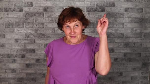 A beautiful mature woman in casual clothes is smiles and raises her index finger up on a brick background. A grown woman was visited by inspiration. The concept of great idea. — Stock Video