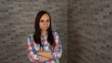 Ekose gömlekli güzel bir genç kadın tuğla bir arka planda protesto etmek için başını sallıyor. Bir kadın reddetme jesti yapar. Genç bir kadının portresi. Vücut dili ve jestler. Başını sallıyor.