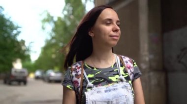 Gündelik giysiler içinde güzel bir genç kadın sokakta gülümsüyor. Uzun saçlı esmer rüzgârda gelişiyor..