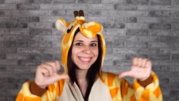 Pyžamo ve formě žirafy. emocionální portrét ženy na šedém cihlovém pozadí. blázen a vtipálek v obleku. animátor pro dětské večírky. Halloween mejdan kostým — Stock video
