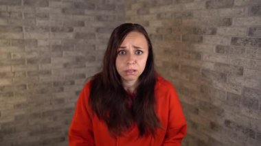 Kırmızı kapüşonlu genç bir kadın tuğladan bir arka planda korku gösteriyor. Bir kadın korkuya kapılmıştı..