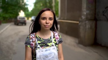 Gündelik giysiler içinde güzel bir genç kadın sokakta gülümsüyor. Uzun saçlı esmer rüzgârda ağır çekimde gelişir..