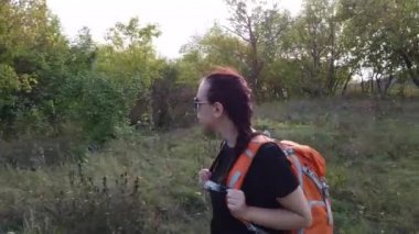 Sırt çantalı genç bir kadın parkta yürüyor.
