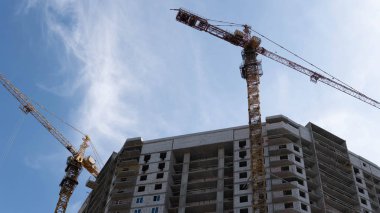 Vinçle inşa edilmiş modern bir bina. Gökyüzünün altında yüksek vinçle inşa edilen binanın altından.