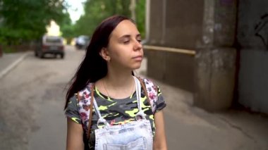Gündelik giysiler içinde güzel bir genç kadın sokakta gülümsüyor. Uzun saçlı esmer rüzgârda ağır çekimde gelişir..