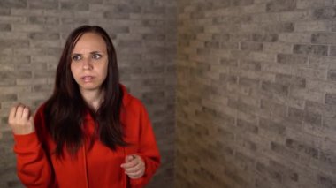 Kırmızı kapüşonlu güzel, duygusal bir kadın şüpheli bir şekilde tuğla arka planda etrafına bakıyor..