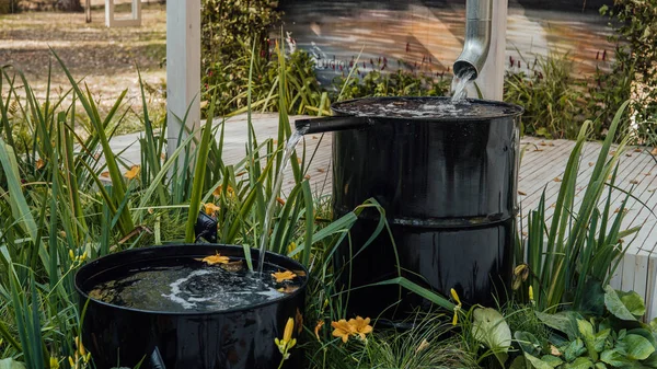 Regenwasser fließt im Sommer aus einem Abflussrohr in die Metalltonne im Garten — Stockfoto