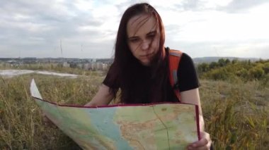 Doğada haritası olan gezgin bir kadın. Sırt çantalı bir kadın dar, dolambaçlı bir yolda yürüyor yeşil çalıların ve ağaçların arasından geçiyor. Sırt çantası taşıyan sıradan bir kadın. Gezgin yalnız seyahat ediyor.