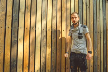 Sıradan giysiler içinde zayıf yapılı genç yakışıklı bir adam ahşap bir çite karşı poz veriyor..