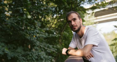 Parktaki yeşil ağaçların arka planında sakallı yakışıklı bir adamın portresi..