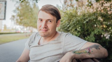 Gündelik giysiler içinde genç yakışıklı bir adam küçük bir sokakta bankta oturuyor..