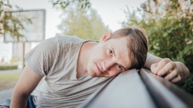 Gündelik giysiler içinde genç yakışıklı bir adam küçük bir sokakta bankta oturuyor..