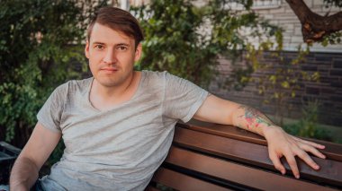 Gündelik giysiler içinde genç yakışıklı bir adam küçük bir sokakta bankta oturuyor..