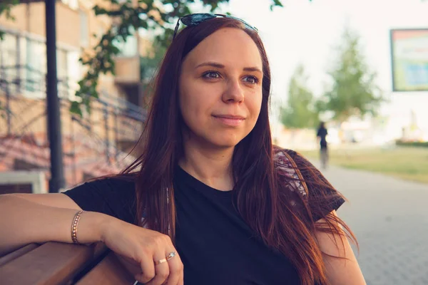 Un retrato de una joven guapa está sentado en un banco en una callejuela pequeña.. — Foto de Stock