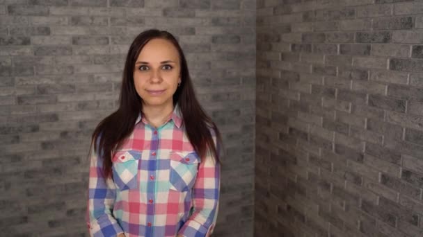 격자무늬 셔츠를 입은 아름다운 젊은 여자 가행 복하게 웃으며 벽돌 배경에 긍정적 인 감정을 표현 한다. — 비디오