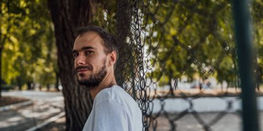 Parktaki tel örgülerin yanında sakallı yakışıklı bir adamın portresi..