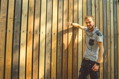 Sıradan giysiler içinde zayıf yapılı genç yakışıklı bir adam ahşap bir çite karşı poz veriyor..