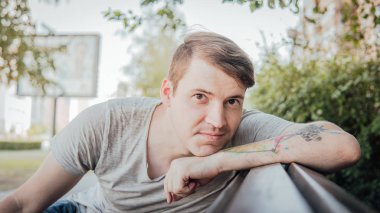 Gündelik giysiler içinde genç yakışıklı bir adam küçük bir sokakta bankta oturuyor..