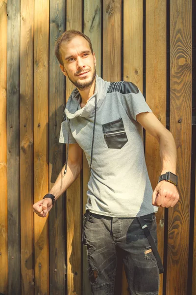 Sıradan giysiler içinde zayıf yapılı genç yakışıklı bir adam ahşap bir çite karşı poz veriyor..