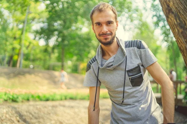 Un retrato de un hombre guapo con barba sobre el fondo de árboles verdes en el parque . — Foto de Stock