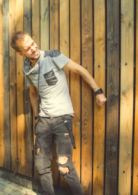 Sıradan giysiler içinde zayıf yapılı genç yakışıklı bir adam ahşap bir çite karşı poz veriyor..