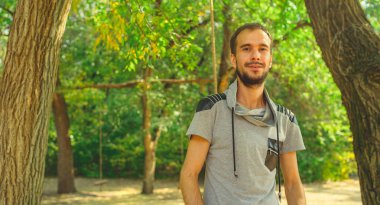 Parktaki yeşil ağaçların arka planında sakallı yakışıklı bir adamın portresi..