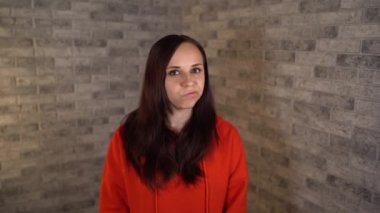 Kırmızı kapüşonlu güzel bir kadın tuğla arka planda protesto etmek için başını sallıyor. Bir kadın reddetme jesti yapar. Genç bir kadının portresi. Vücut dili ve jestler. Başını sallıyor.